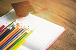 colorato matita impostato e la laurea berretto su bianca carta taccuino indietro per scuola e formazione scolastica concetto - pastelli colorato foto