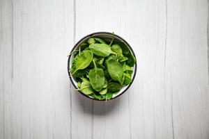 fresco spinaci le foglie nel ciotola su rustico di legno tavolo. superiore Visualizza. foto