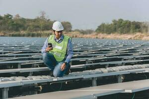 ingegnere ispettore Tenere il computer portatile e Lavorando nel solare pannelli energia pianta controllo fotovoltaico cellule e elettricità produzione. foto