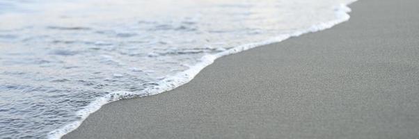 onda sfocata del mare sulla spiaggia di sabbia di sera foto