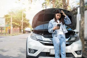 donna asiatica arrabbiata e utilizzando il telefono cellulare per chiedere assistenza dopo un guasto alla macchina in strada. concetto di problema al motore del veicolo o incidente e aiuto di emergenza da un meccanico professionista foto