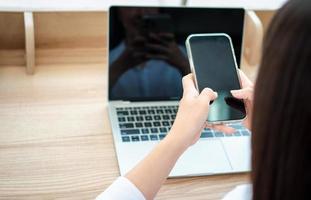 felice bella donna asiatica che lavora su un laptop e smartphone presso l'ufficio a casa seduto al tavolo. felice libero professionista femminile online utilizzando il concetto di notebook e smartphone. foto