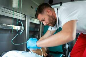 paramedico assistenza sanitaria emergenza personale assunzione cura di un' dire bugie giù giovane donna paziente su barella con medico ventilatore sistema e borsa-valvola maschere dentro un medico servizio ambulanza macchina. foto