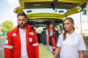 giovane paramedici in movimento ambulanza barella a partire dal macchina. paramedici nel uniforme assunzione barella su il ambulanza auto foto