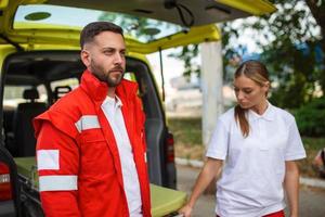 giovane paramedici in movimento ambulanza barella a partire dal macchina. paramedici nel uniforme assunzione barella su il ambulanza auto foto