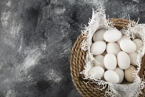 un cesto di legno pieno di uova di gallina crude bianche foto
