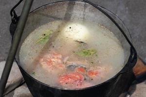delizioso rosso salmone pesce fresco-soup cucinato nel grande giocatore di bowling su fuoco di bivacco all'aperto foto