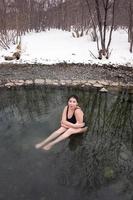 grande dimensione giovane modello nel nero bagnarsi costume da bagno seduta nel all'aperto piscina a terme, inverno indurimento foto