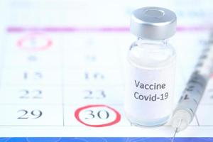 primo piano del vaccino contro il coronavirus e la siringa su un calendario con un cerchio rosso