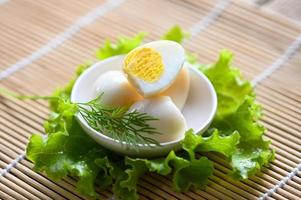 bollito uova cibo, Quaglia uova su bianca ciotola, prima colazione uova con fresco Quaglia uova e verdura lattuga su tavolo sfondo foto