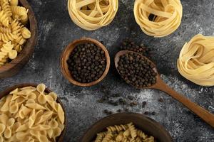 pasta secca e grani di pepe nero su fondo in marmo foto