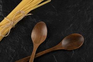 spaghetti crudi e cucchiai di legno su uno sfondo nero foto