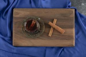 un tè di vetro con bastoncini di cannella su un tagliere di legno foto