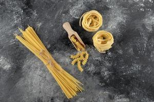 nidi di tagliatelle, spaghetti e fusilli su fondo di marmo foto