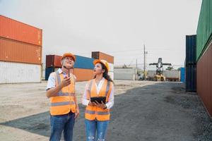 Due asiatico industriale ingegnere uomo e donna indossare sicurezza veste e casco. caposquadra parlando con lavoratore o lavoratore nel il industriale contenitore carico. foto