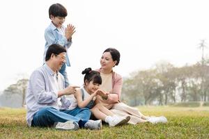 Immagine di un asiatico famiglia seduta insieme su il erba a il parco foto