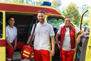 tre paramedici di il ambulanza. giovane donna e uomo sorridente. medico è trasporto un' medico trauma Borsa. foto