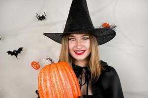 Halloween bandiera con contento femmina vestiti come un' strega Tenere zucca su sfondo con ragnatela foto