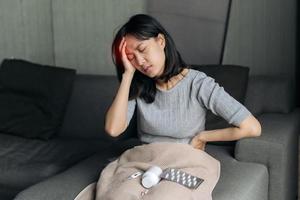asiatico donna ha un' mal di testa su divano letto. femmina Tenere doloroso testa. persone con testa problema, assistenza sanitaria e medicinale. foto