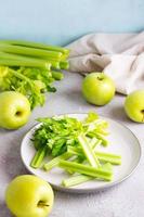 affettato fresco sedano gambo con le foglie su un' piatto e verde mele su il tavolo pronto per essere cucinato. vegetariano cibo. verticale Visualizza foto