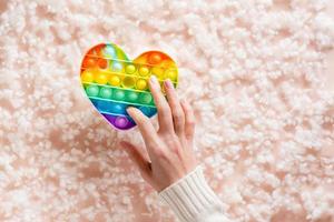 un' femmina mano presse un' silicone arcobaleno anti stress giocattolo su un' sfondo di lanugine. un' moderno modo per rilassare foto