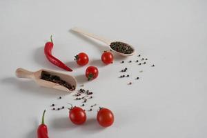 ciliegia pomodori, rosso caldo chili Pepe, fragrante nero Pepe piselli su un' bianca sfondo. sfondo con spezie. piatto posizione, copia spazio foto