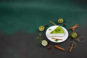 torta di formaggio con kiwi, cannella bastone e le foglie menta su un' verde sfondo. copia cpase per testo foto