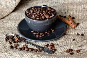 tazza di caffè nero piena di chicchi di caffè biologico e bastoncini di cannella su un panno di lino
