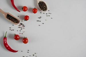 ciliegia pomodori, rosso caldo chili Pepe, fragrante nero Pepe piselli su un' bianca sfondo. sfondo con spezie. piatto posizione, copia spazio foto