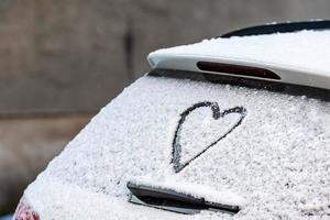 a forma di cuore sul lunotto della macchina coperta di neve