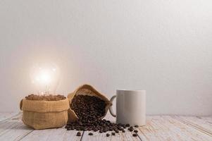 una tazza di caffè con sacchi di chicchi di caffè e una lampadina che emette energia su un tavolo di legno foto