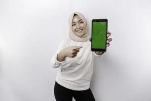 un' contento asiatico musulmano donna indossare un' foulard, mostrando sua Telefono schermo, isolato di bianca sfondo foto