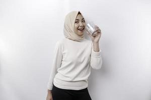 gioioso asiatico musulmano donna indossare foulard è potabile un' bicchiere di acqua, isolato su bianca sfondo. foto