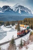 moranti curva con iconico rosso carico treno passaggio attraverso arco valle e roccioso montagne nel inverno a Banff nazionale parco foto