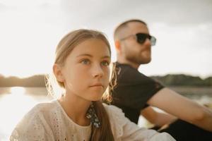 un ritratto ravvicinato di una giovane ragazza che posa con il padre con la barba e gli occhiali da sole sulla costa foto