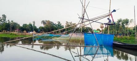 un' pescatore pesca con bambù e netto trappola, un' pescatore pesca con bambù e netto trappola, villaggio lago barca acqua verde albero blu cielo foto