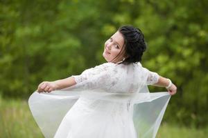 ritratto di un' paffuto sposa con un' agitando velo contro un' sfondo di estate verde. foto