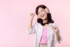 Sorridi bella asiatico modello persona ascolta musica canzone e godere danza con senza fili cuffie in linea Audio Radio suono. positivo divertimento Uscito gioioso gioventù femmina donna su rosa isolato sfondo studio foto