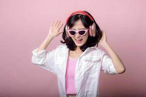 contento giovane asiatico donna modello con elegante di moda sole bicchieri godere ascoltando musica di cuffie Audio e danza isolato su rosa studio sfondo. tecnologia, ragazza moda, accessorio concetto.