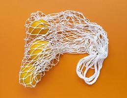 Borsa eco in cotone bianco stringa con arance all'interno su uno sfondo arancione, monocromatico piatto semplice ecologia laici concetto di rifiuti zero
