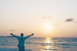 un uomo che alza le mani al cielo in spiaggia durante le vacanze estive
