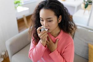 asiatico donna utilizzando inalatore mentre sofferenza a partire dal asma a casa. giovane donna utilizzando asma inalatore. avvicinamento di un' giovane asiatico donna utilizzando asma inalatore a casa. foto