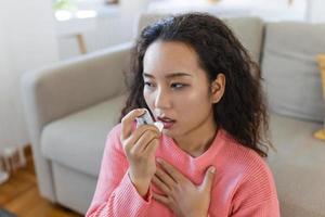 asiatico donna utilizzando inalatore mentre sofferenza a partire dal asma a casa. giovane donna utilizzando asma inalatore. avvicinamento di un' giovane asiatico donna utilizzando asma inalatore a casa. foto