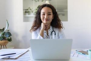 medico professionale femmina asiatico medico indossare uniforme assunzione Appunti nel medico rivista, Riempimento documenti, paziente malattia storia, guardare a il computer portatile schermo, alunno Guardando seminario web foto