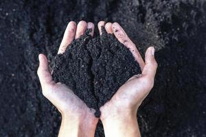 mani Tenere abbondanza suolo per agricoltura o preparazione per pianta analisi suolo campioni su mani con suolo terra sfondo. sporco qualità e agricoltura concetto. selettivo messa a fuoco su nero suolo nel davanti foto