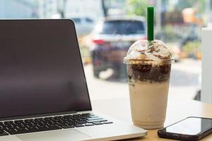 ghiaccio biscotti e crema, ghiaccio latte cioccolato su il tavolo, frullato frappè con trasparente bicchiere nel bar, ghiaccio latte con frustato crema, completare con computer portatile, smartphone nel opera, studia, e attività commerciale foto