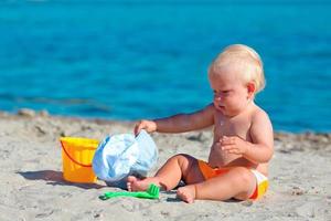 bambino piccolo seduta su il spiaggia e giocando con plastica giocattoli nel il sabbia. foto