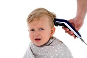 femmina mani tagliare un' pianto bambino con un elettrico capelli clipper nel un' parrucchiere. primo taglio di capelli. foto