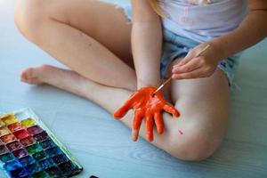 il bambino si siede su il pavimento e vernici il suo palma con arancia dipingere. quarantena. foto