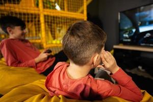 Due fratelli giocando gara video gioco console, seduta su giallo pouf nel bambini giocare centro. foto